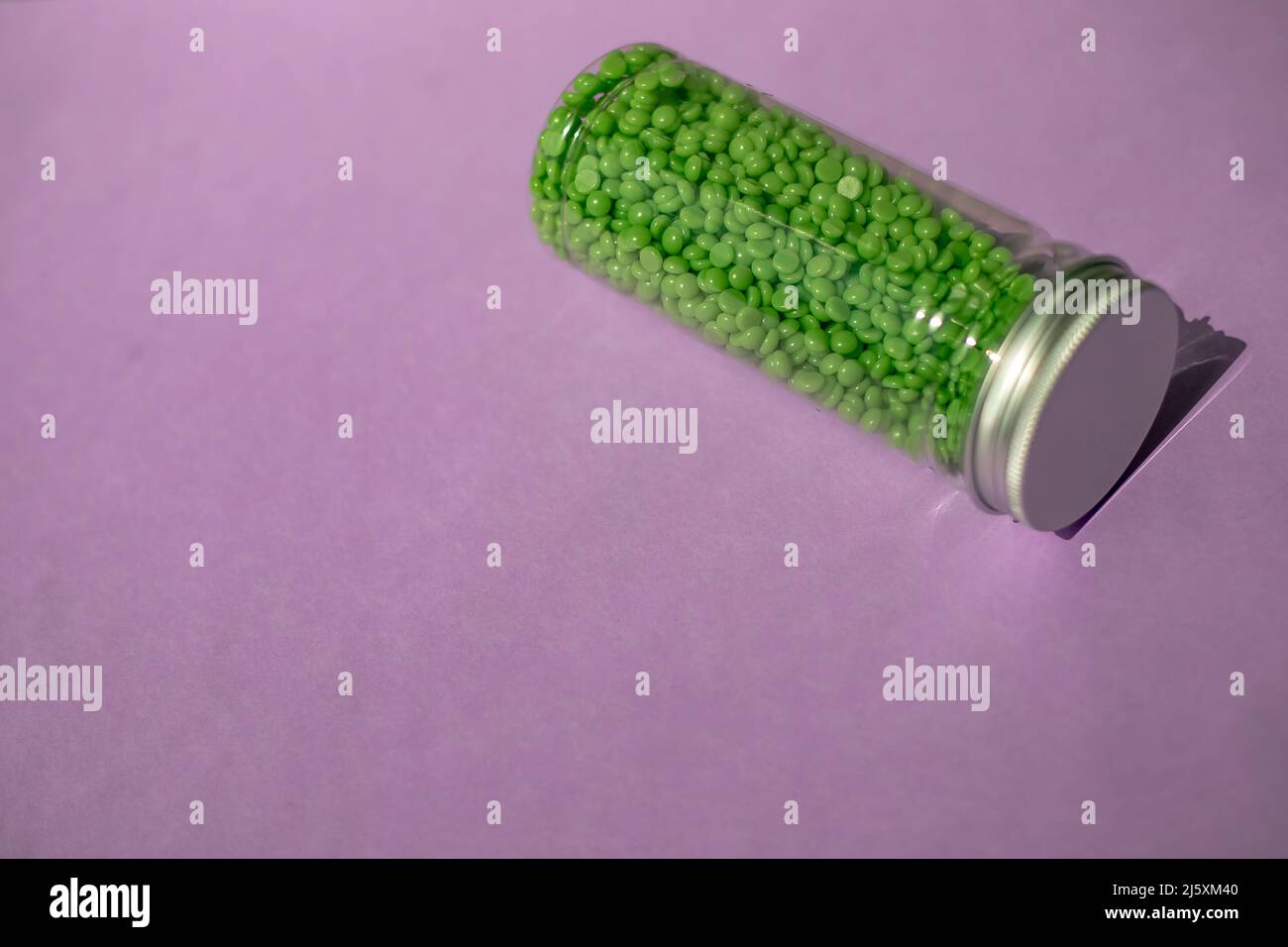 cire verte pour l'épilation en granules. sur fond violet. pot avec cire sur fond isolé Banque D'Images