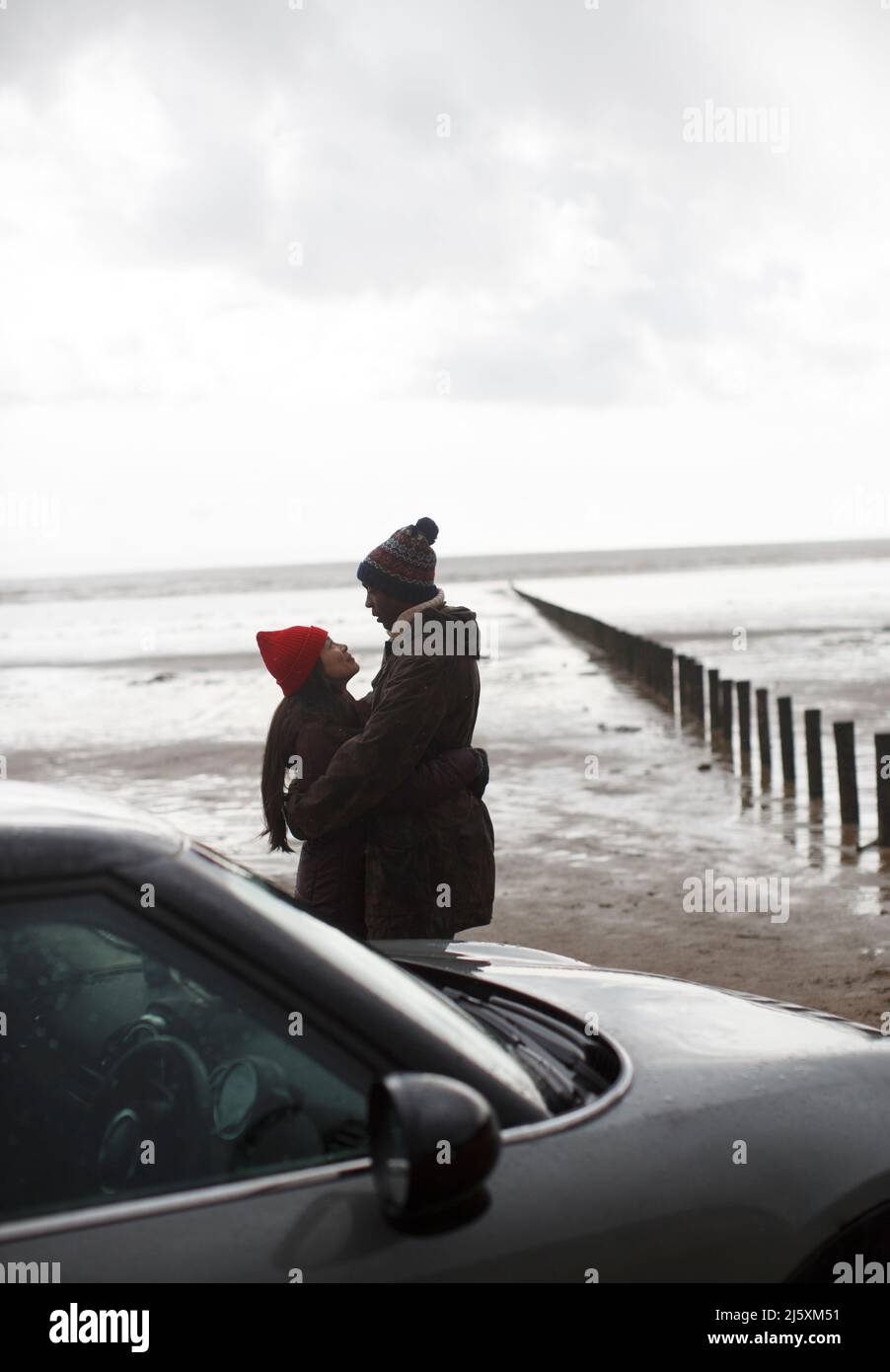 Un couple affectueux en vêtements chauds qui s'embrasse sur la plage humide d'hiver Banque D'Images