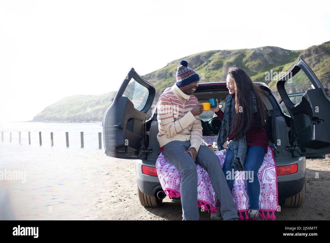 Un couple heureux qui boit du café à l'arrière de la voiture sur la plage d'hiver Banque D'Images