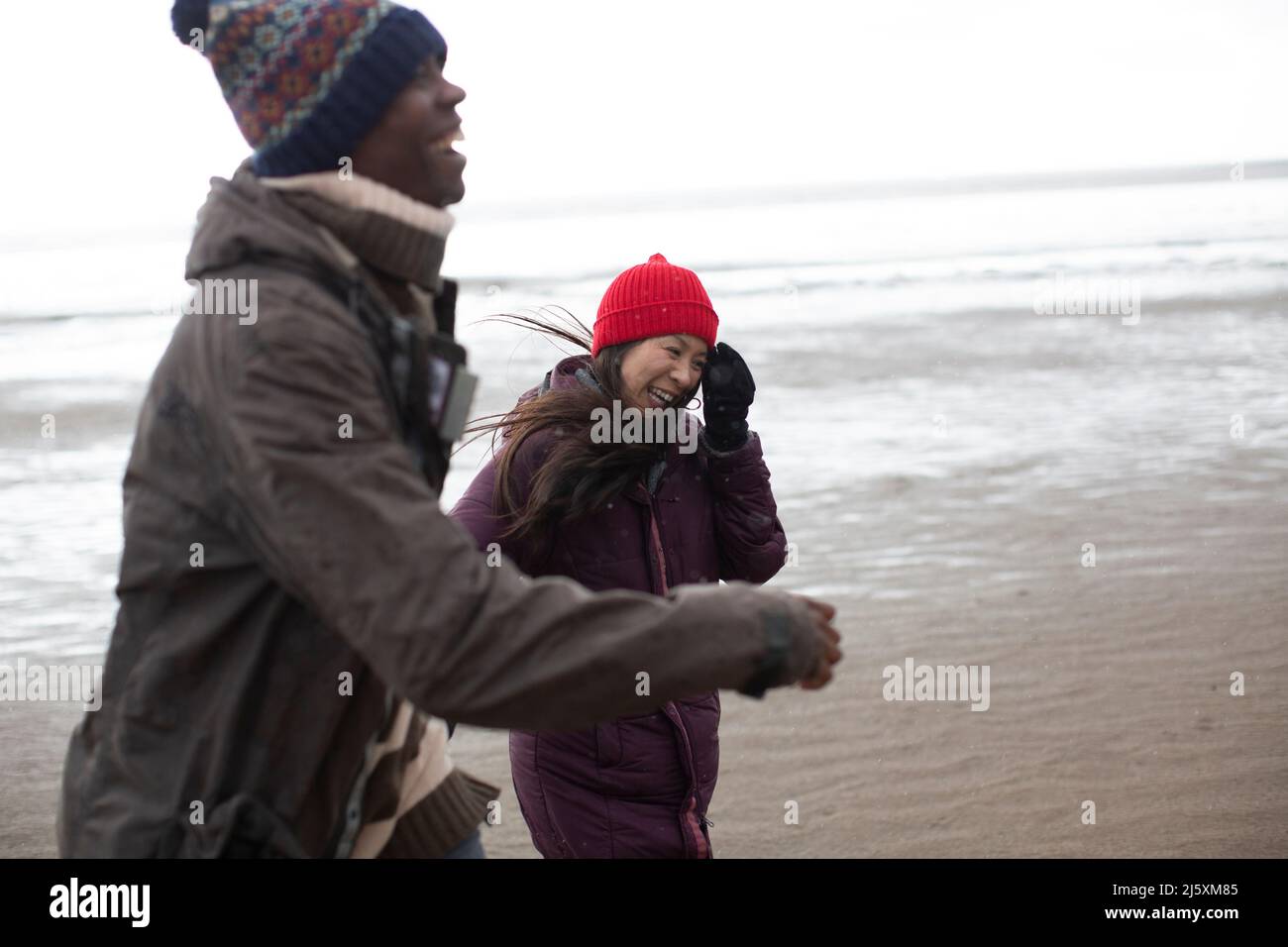 Couple heureux en vêtements chauds sur la plage humide d'hiver Banque D'Images
