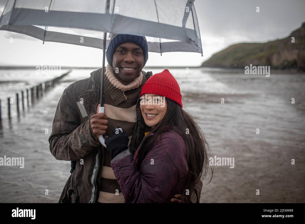 Portrait heureux couple sous parapluie sur la plage humide d'hiver Banque D'Images