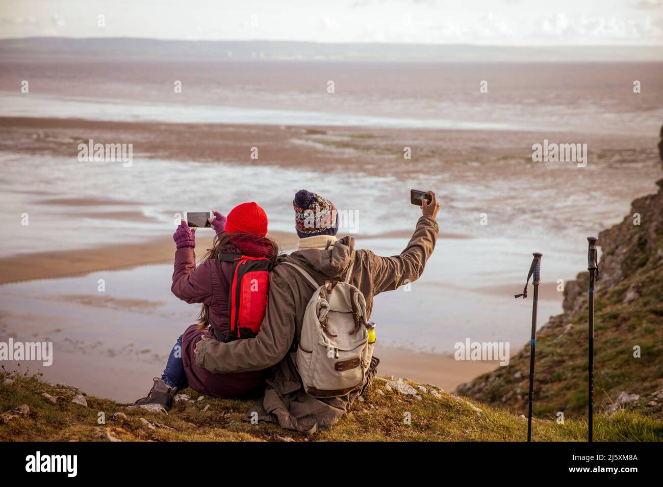 Un couple de randonneurs avec des téléphones à caméra sur la falaise surplombant la plage d'hiver Banque D'Images