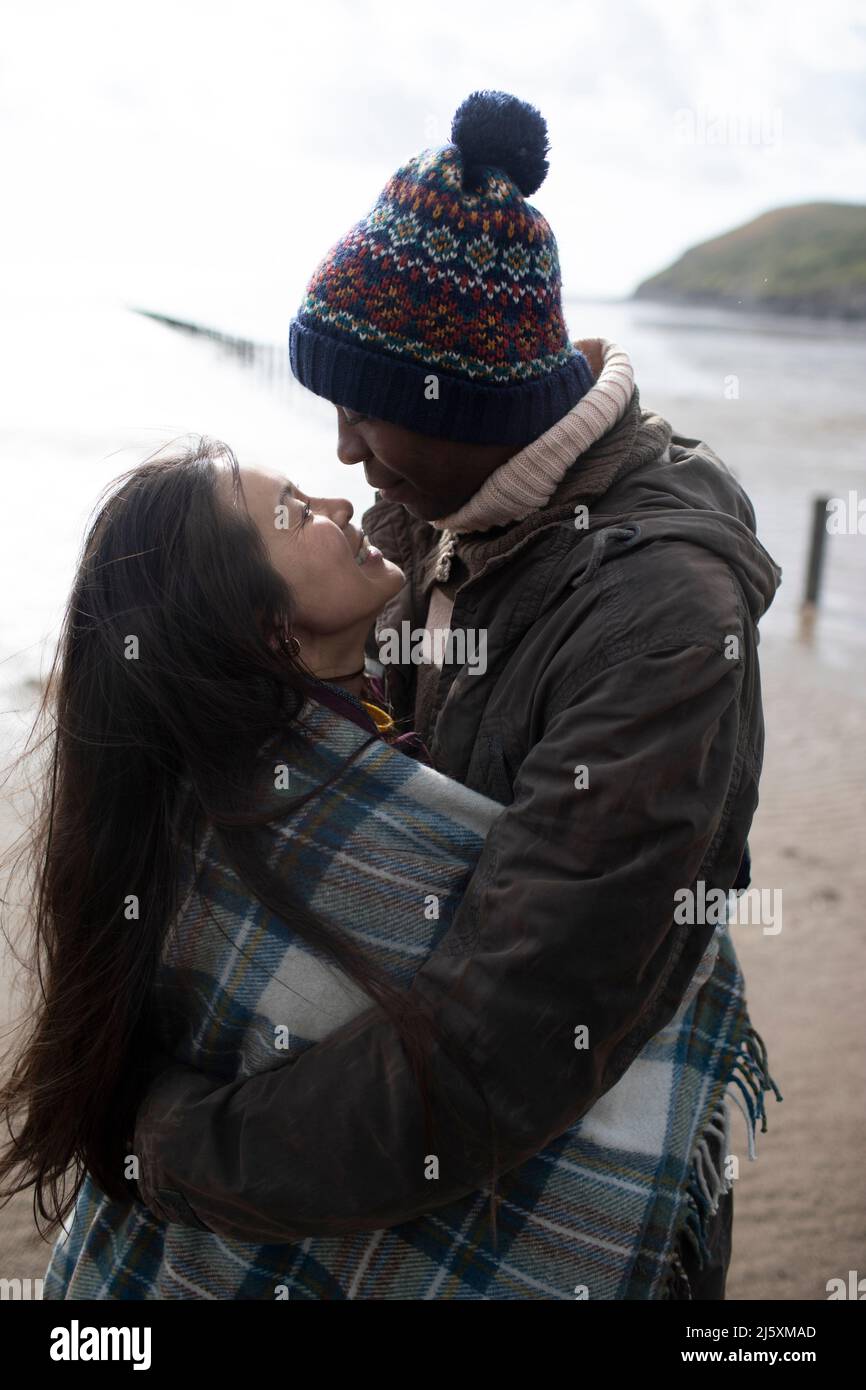 Couple affectueux enveloppé dans une couverture sur la plage d'hiver Banque D'Images