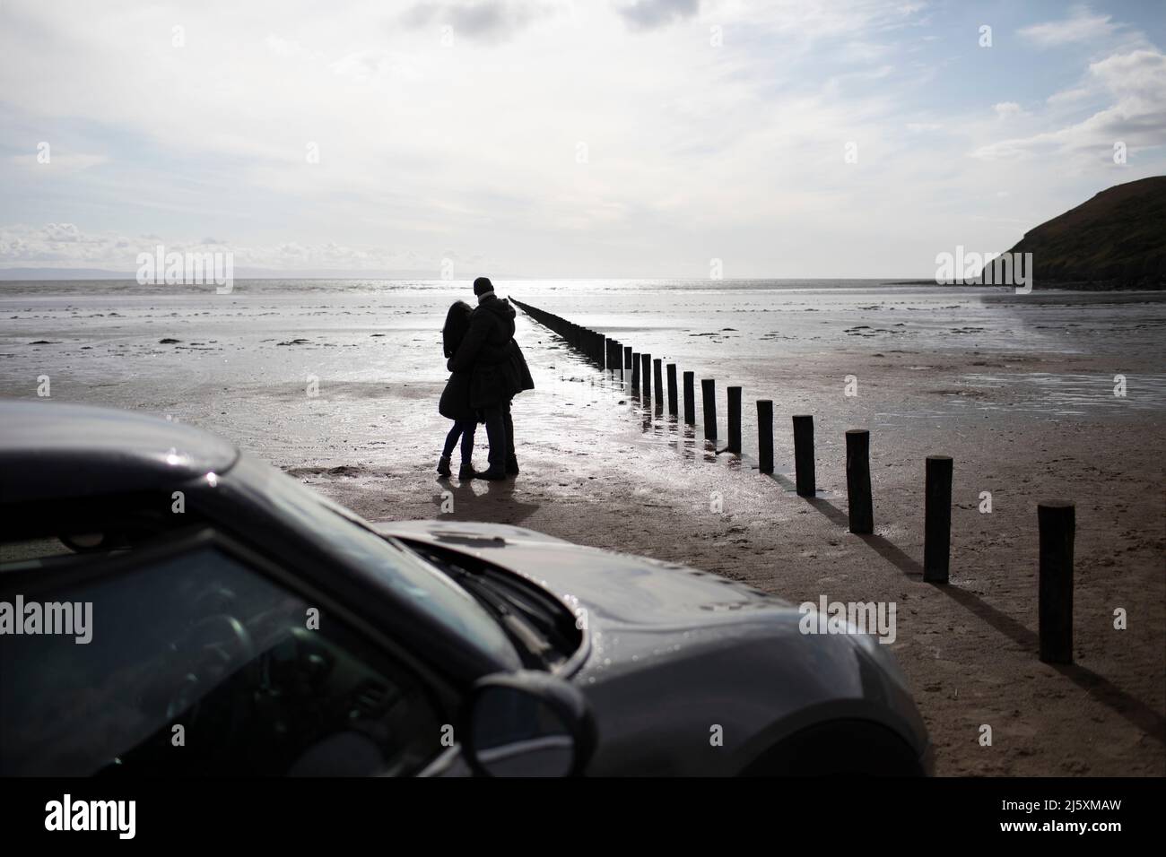Silhouette affectueuse couple qui s'enserre sur la plage ensoleillée d'hiver humide Banque D'Images