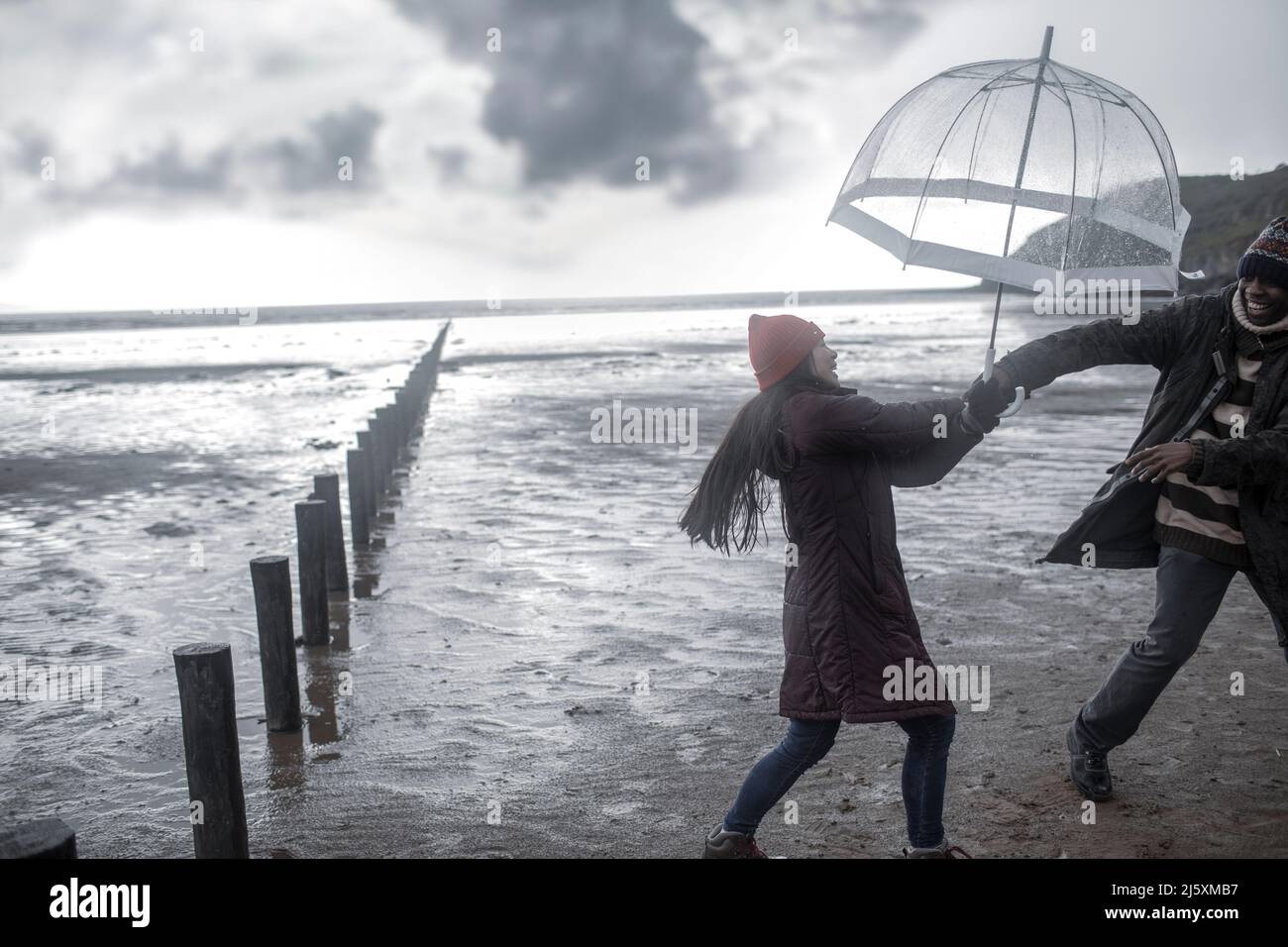 Couple espiègle avec parasol sur la plage humide de l'océan en hiver Banque D'Images