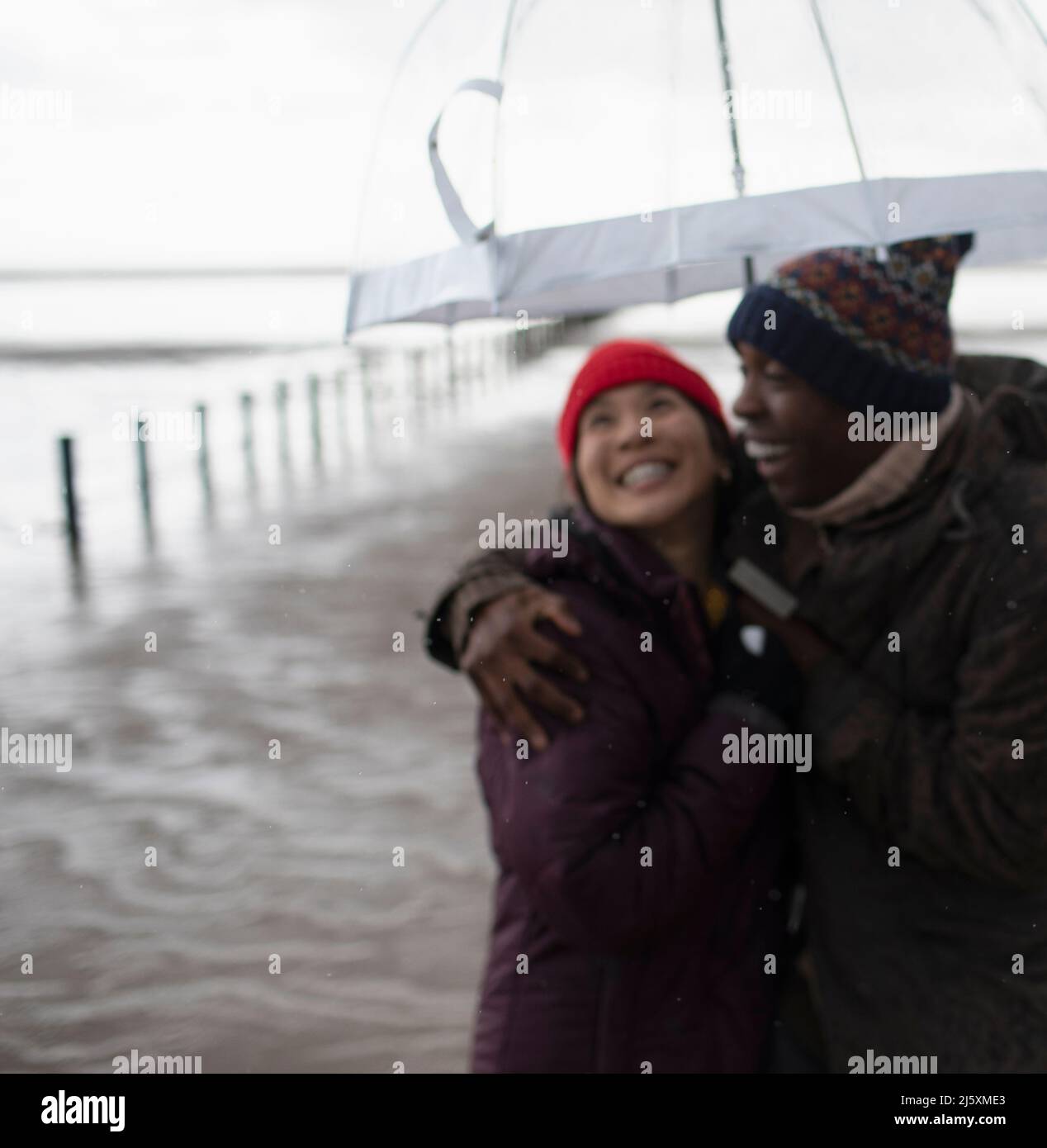 Couple heureux en vêtements chauds sous parapluie sur la plage humide d'hiver Banque D'Images