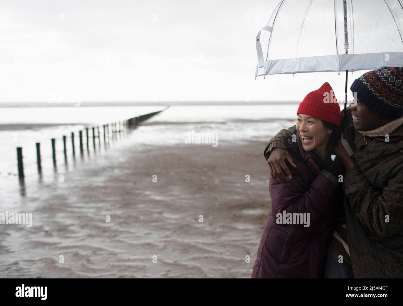 Un couple heureux qui s'enserre sous un parapluie sur une plage humide d'hiver Banque D'Images