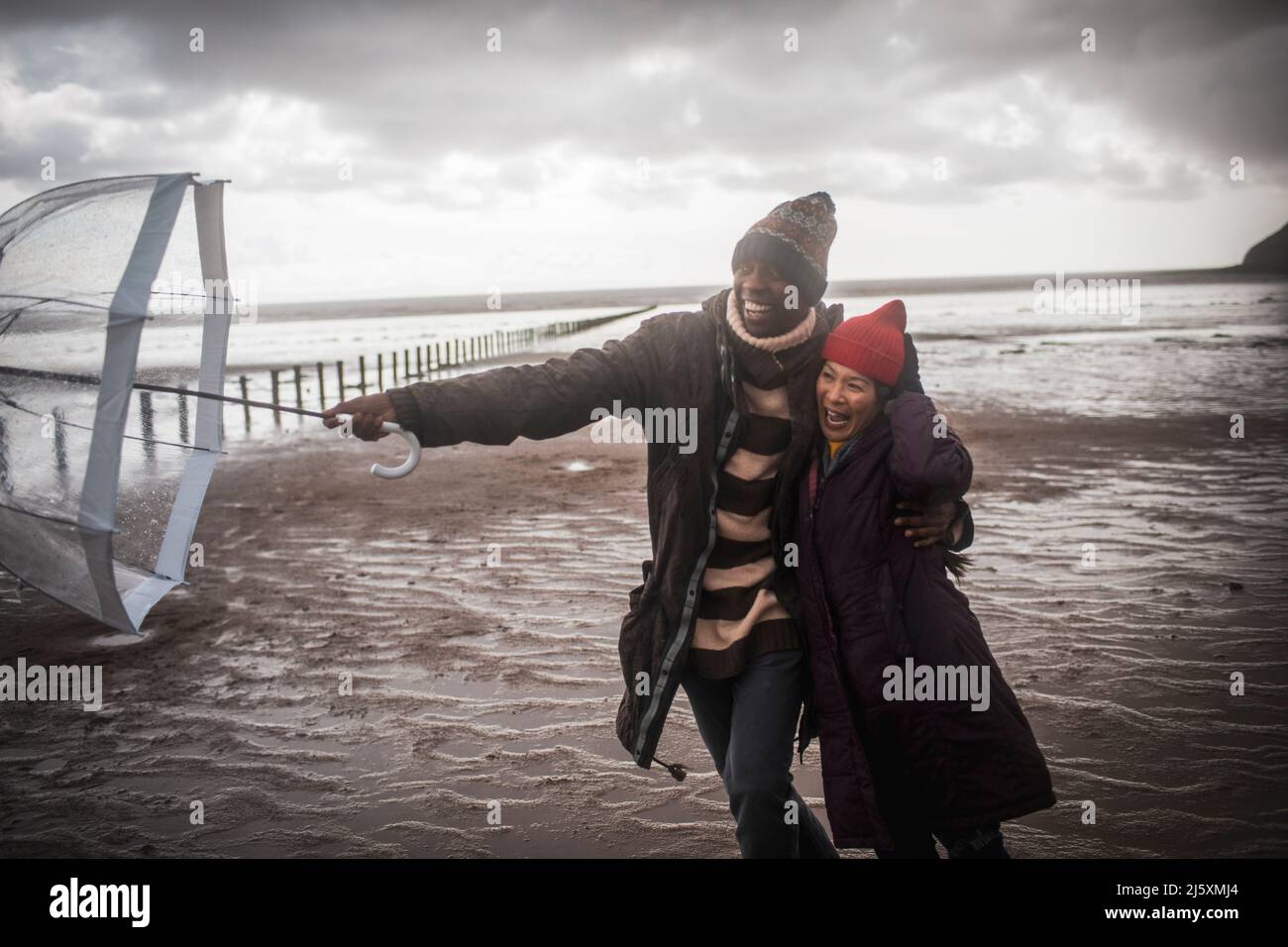 Couple affectueux avec parasol sur la plage humide d'hiver Banque D'Images