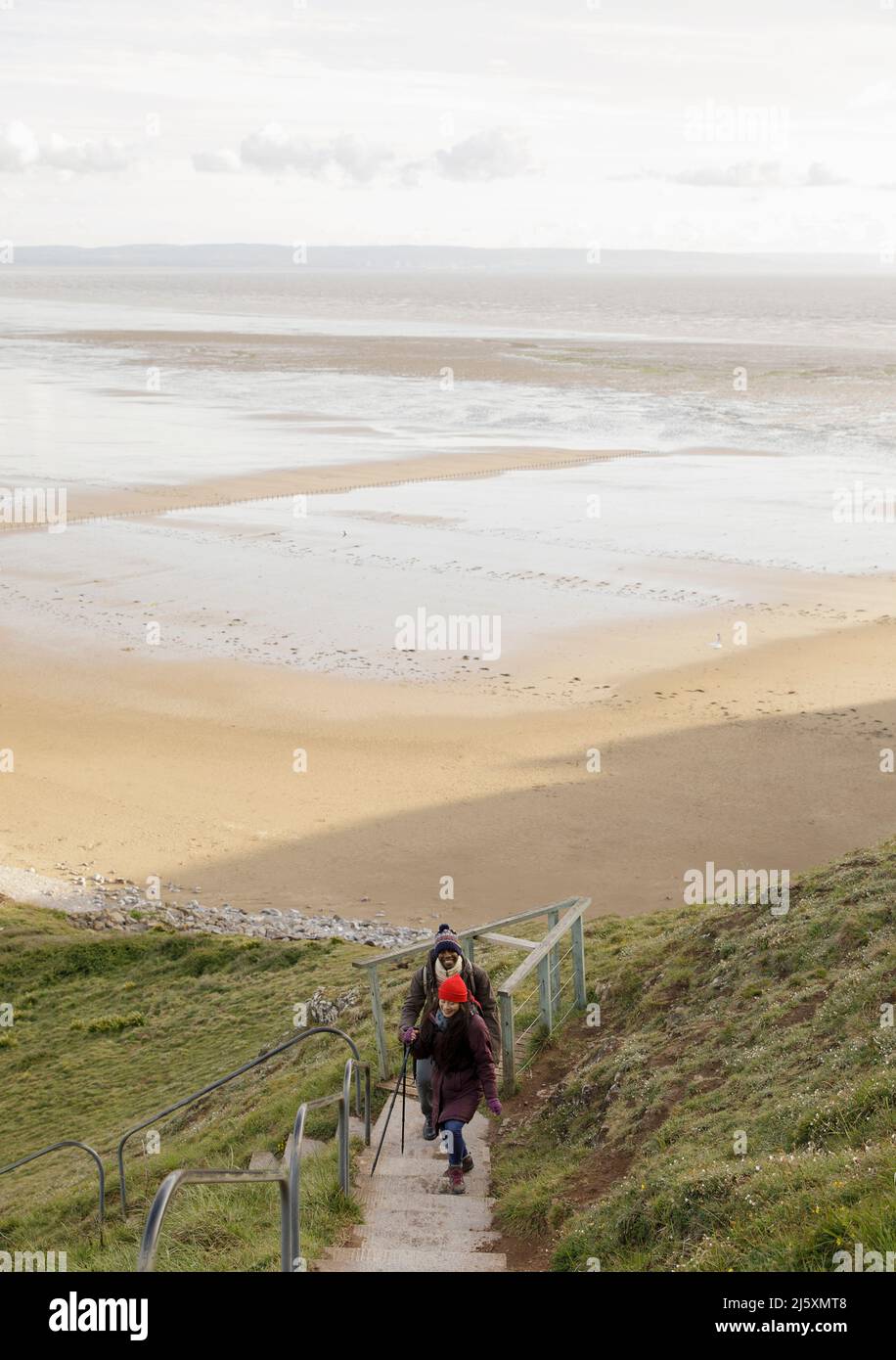 Un couple de randonneurs monte des escaliers de falaise au-dessus de la plage d'hiver sur l'océan Banque D'Images