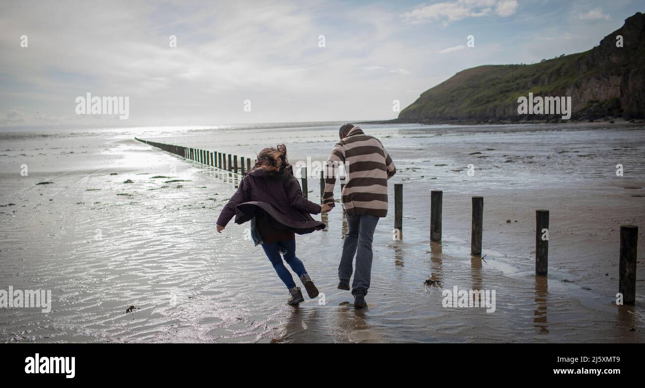 Couple espiègle qui court sur une plage humide en hiver Banque D'Images