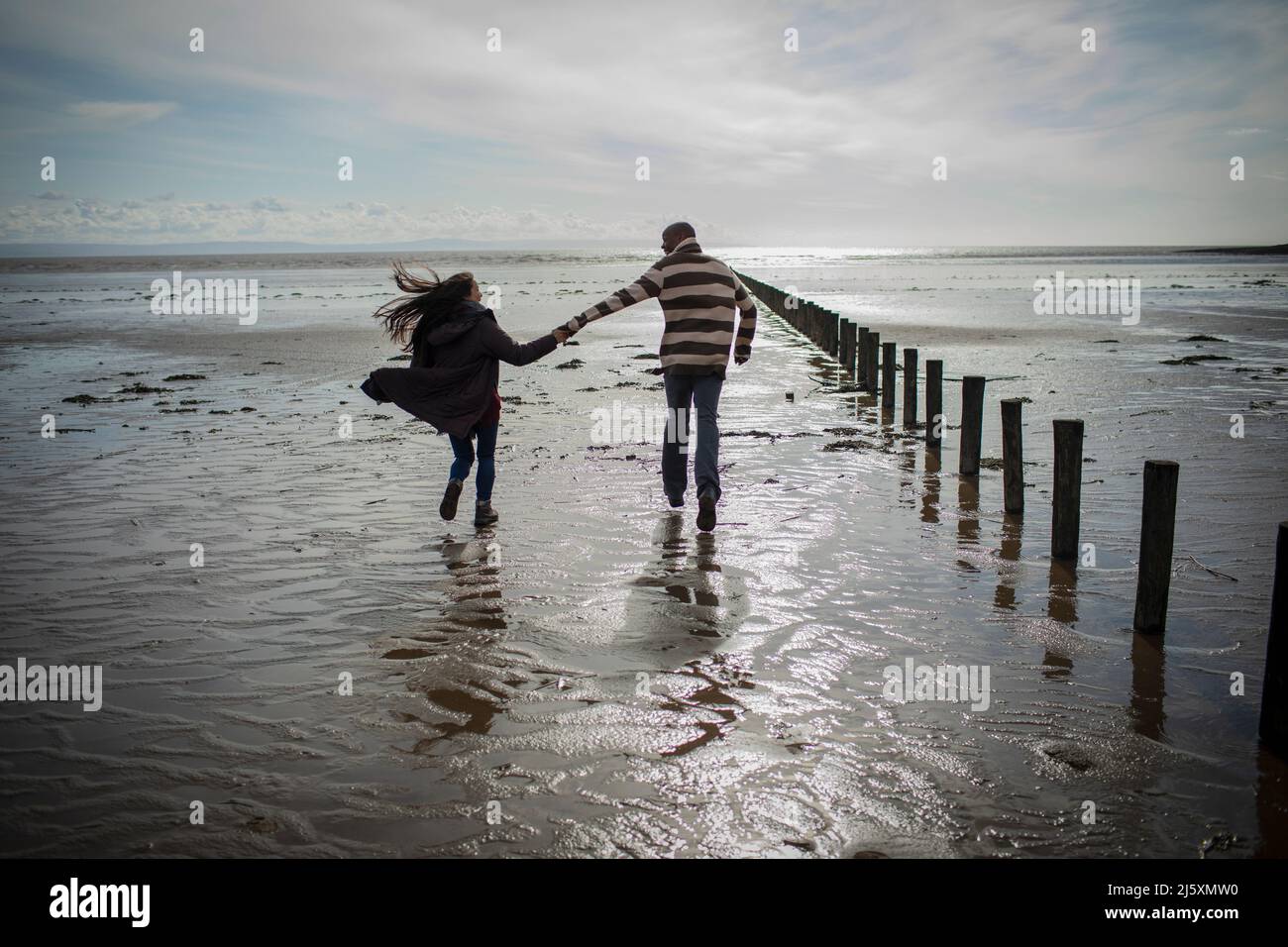 Couple tenant les mains courant sur la plage d'hiver ensoleillée et humide Banque D'Images