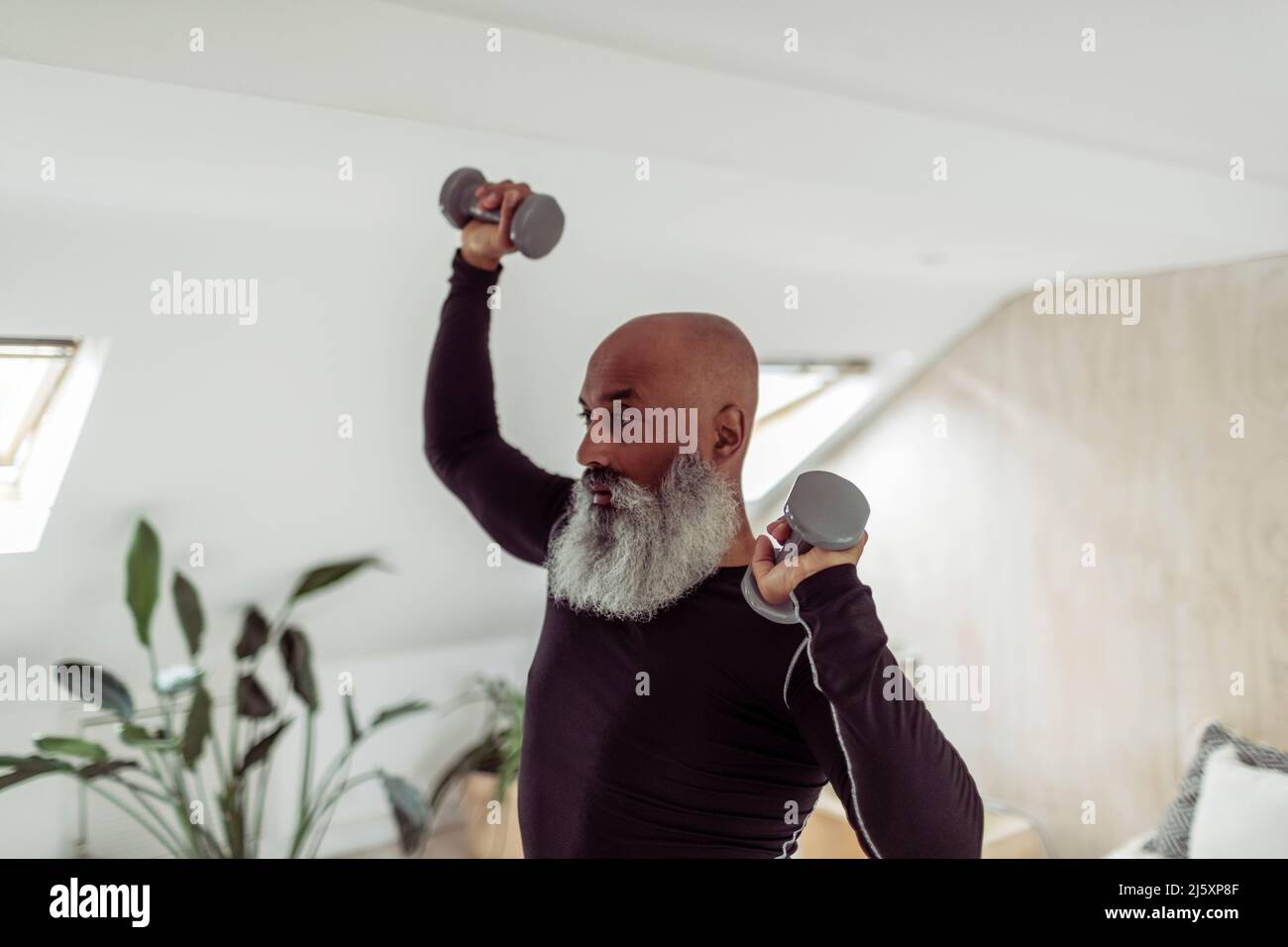 Homme mûr avec la barbe s'exerçant avec des haltères à la maison Banque D'Images