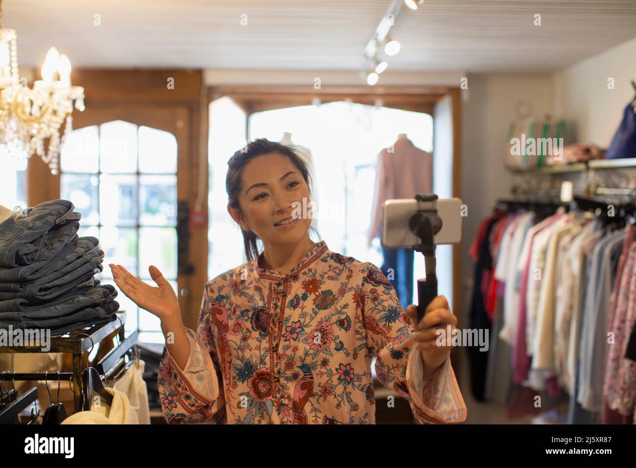 Une femme propriétaire de boutique se vjournalisation avec un smartphone dans une boutique de vêtements Banque D'Images