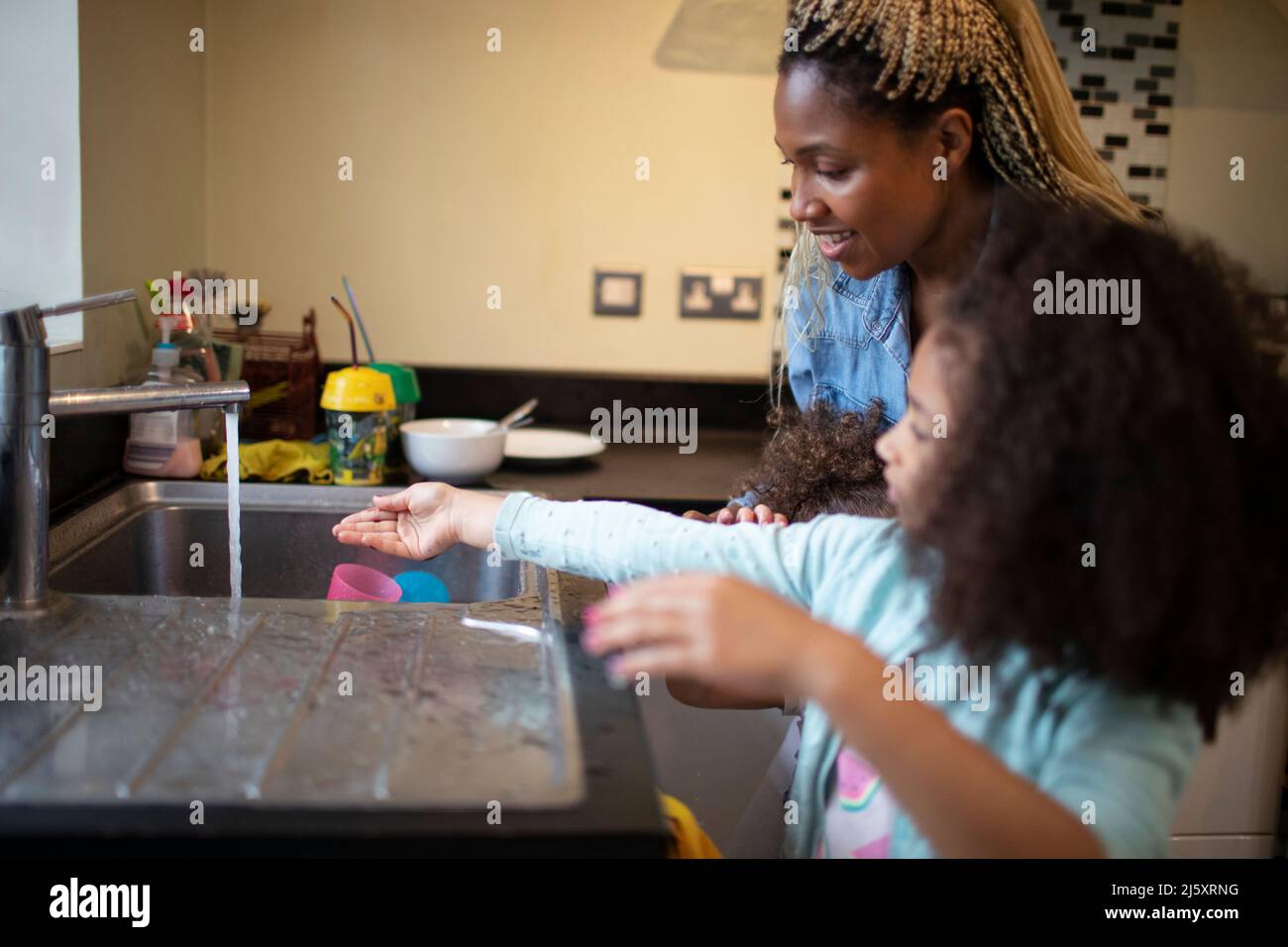 Mère aidant fille se laver les mains à l'évier de cuisine Banque D'Images