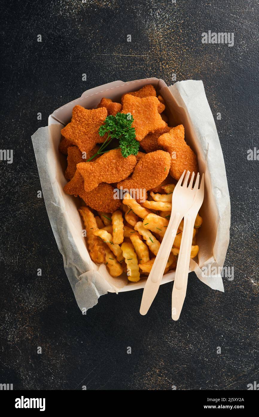 Fish and Chips, restauration rapide britannique. Bâtonnets de poisson avec frites sur une plaque de papier à emporter sur fond de béton ancien sombre. Traditionnel anglais authe Banque D'Images