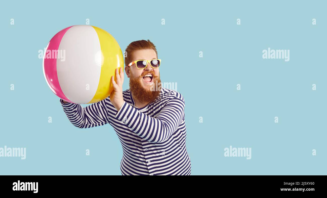Gai drôle gars en lunettes de soleil jouant avec ballon gonflable de plage sur fond bleu pastel. Banque D'Images
