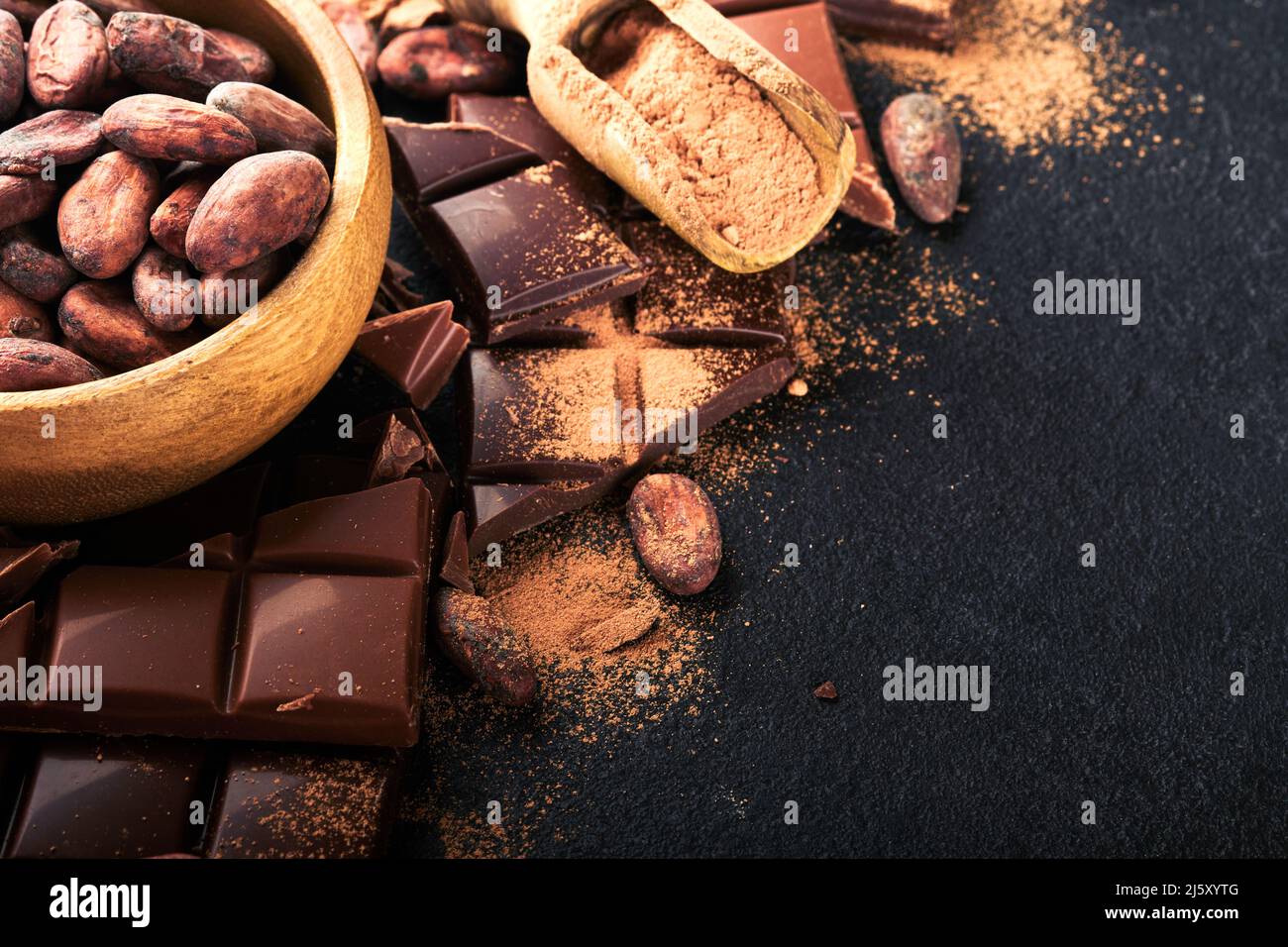 Cacao en grains de chocolat. Composition de cacao en poudre, de barres de cacao en grains et de morceaux de lait et de chocolat noir différents sur fond noir. Cuisson de la Chocola Banque D'Images