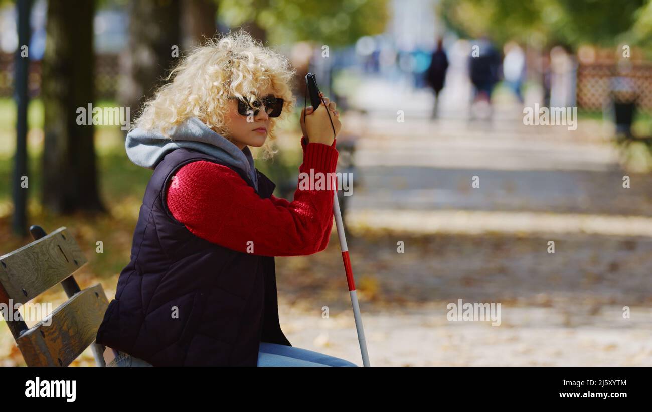 Jeune femme blonde aveugle dans le parc en lunettes avec un bâton de canne moyen espace de copie automne parc arrière-plan . Photo de haute qualité Banque D'Images