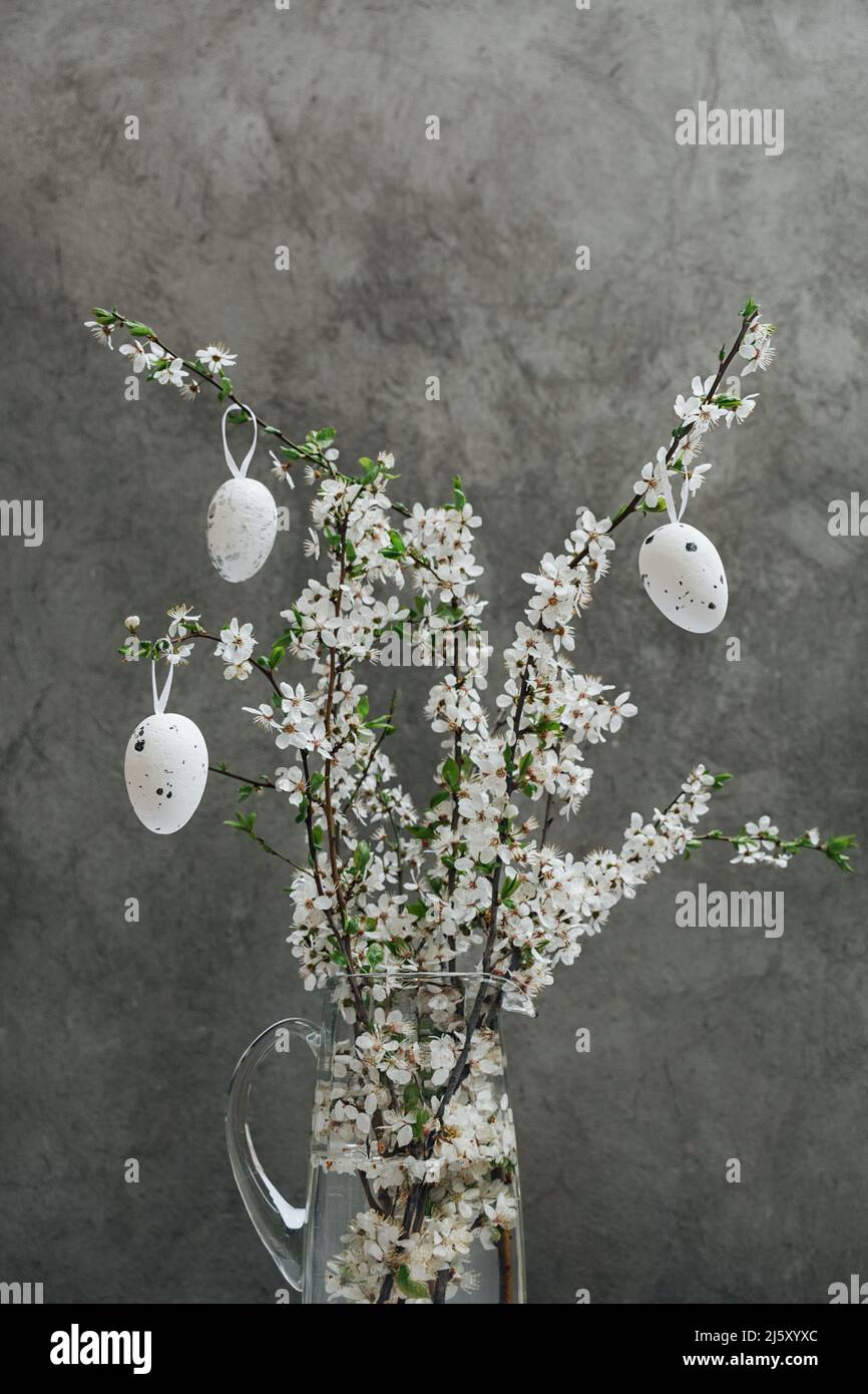 Bouquet de brindilles de cerisier fleuris dans une carafe en verre sur un fond de mur en béton. Photo verticale. Le concept de fleurs dans la ville. Banque D'Images