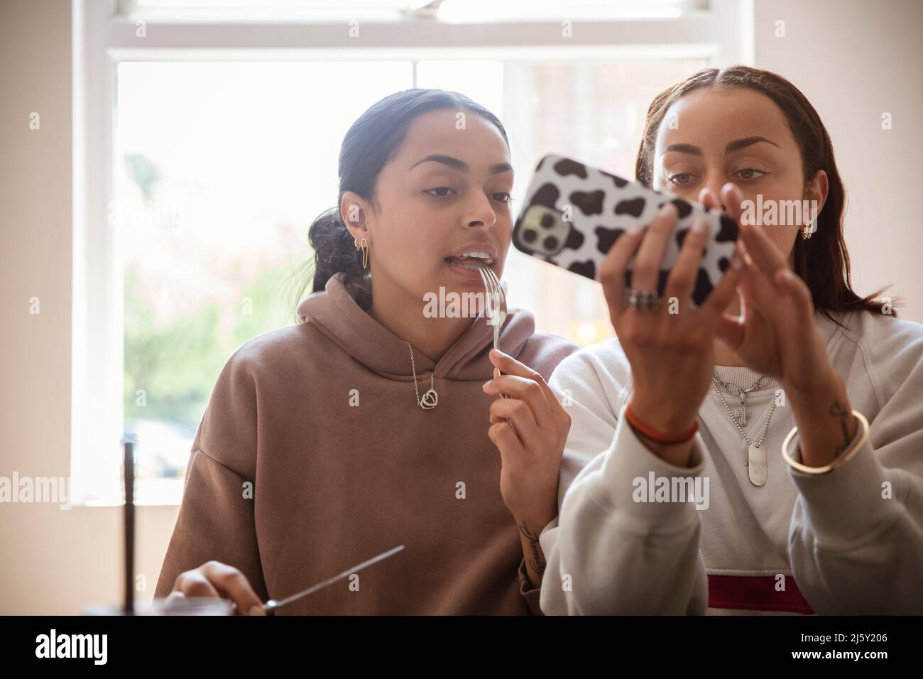 Jeunes sœurs adultes mangeant et utilisant un smartphone Banque D'Images