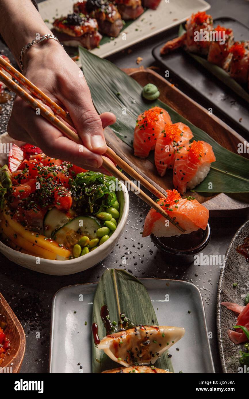 Du haut de la crop-personne avec des baguettes mangeant des sushis avec du saumon et des herbes d'une table avec différents plats d'un restaurant asiatique de luxe Banque D'Images