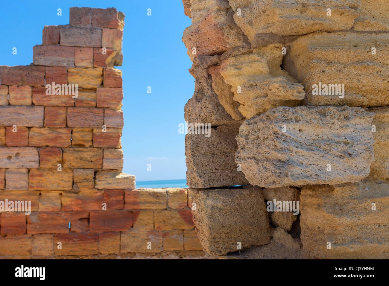 Arrière-plan avec un vieux mur fait de blocs de calcaire de différentes tailles et formes et ciel avec la mer. Banque D'Images