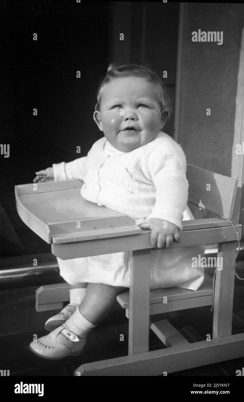 1960, historique, enfant en bas âge assis dans une chaise haute en bois, Angleterre, Royaume-Uni. Banque D'Images