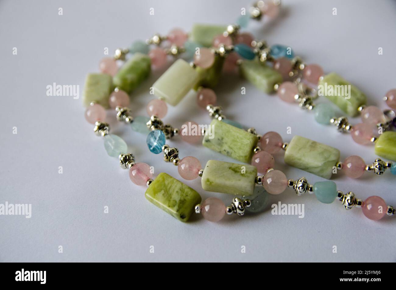 Un collier fait à la main fait de perles de couleur pastel en bleu-vert, de quartz rose et de jade. Vue sur un arrière-plan blanc avec ombre portée. Banque D'Images