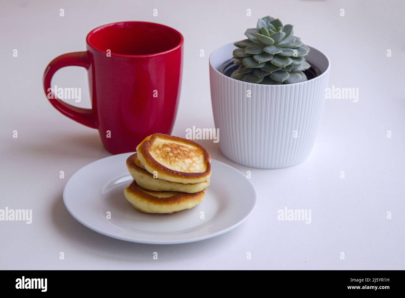 Crêpes maison fraîches et moelleuses sur l'assiette, tasse rouge et plante succulente sur une table Banque D'Images