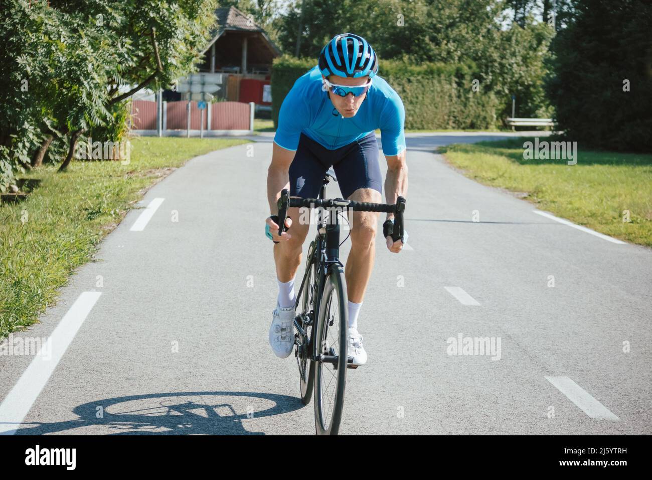 Athlète homme en maillot bleu et en équipement de vélo, en train de monter un cycle de course professionnel sur la route pavée Banque D'Images