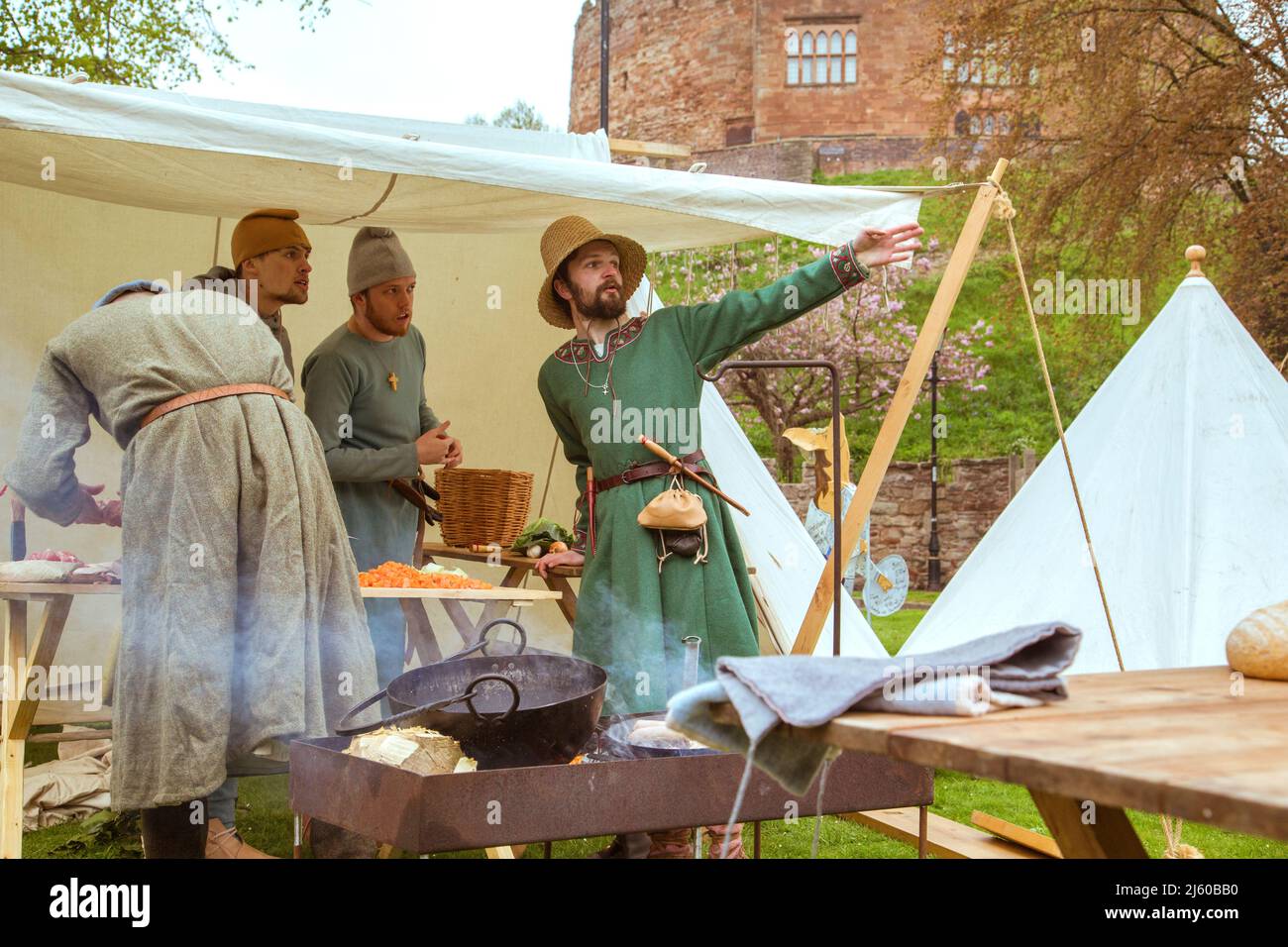 Des amis parlent tout en préparant la nourriture lors d'une reconstitution d'un camp médiéval dans le domaine du château de Tamworth, Angleterre, Royaume-Uni. Banque D'Images