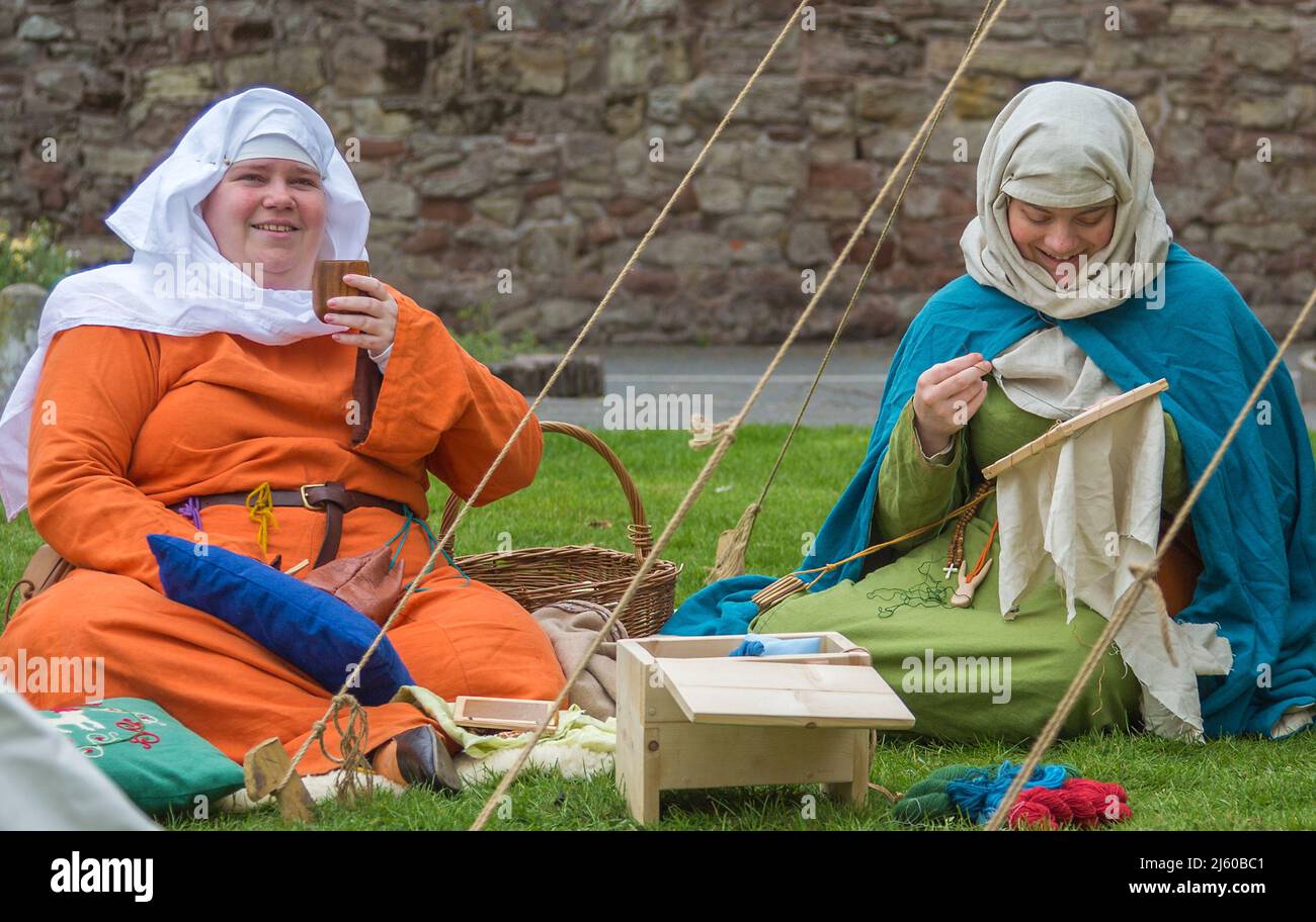 Maidens en costume d'époque s'assoient en croix sur le sol lors d'une reconstitution d'un camp médiéval dans le domaine du château de Tamworth, Angleterre, Royaume-Uni. Banque D'Images