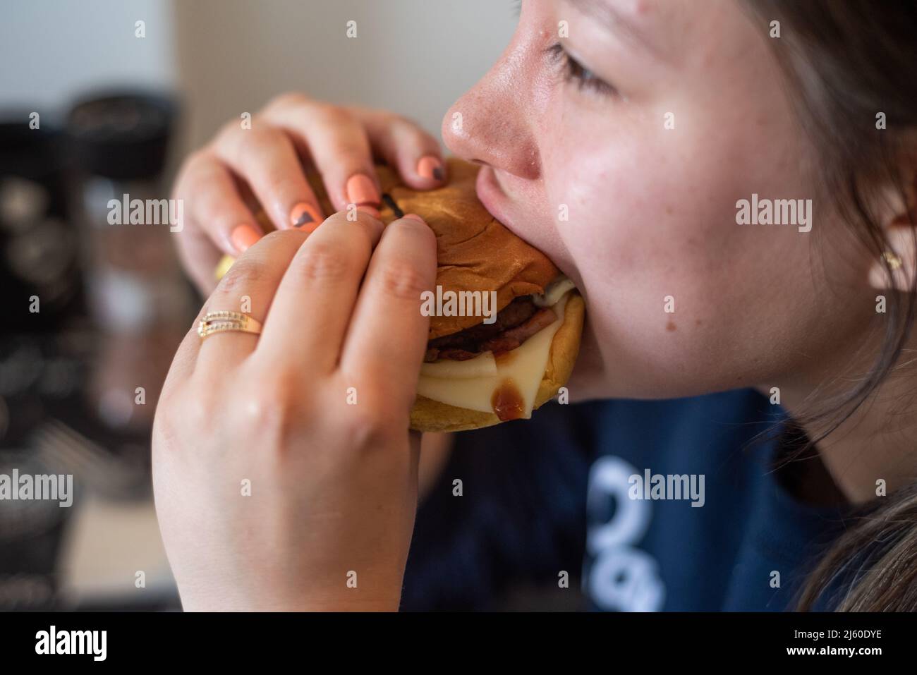 Jeune femme latina mangeant un hamburger fait main avec du bacon, du fromage et de la viande à la maison Banque D'Images