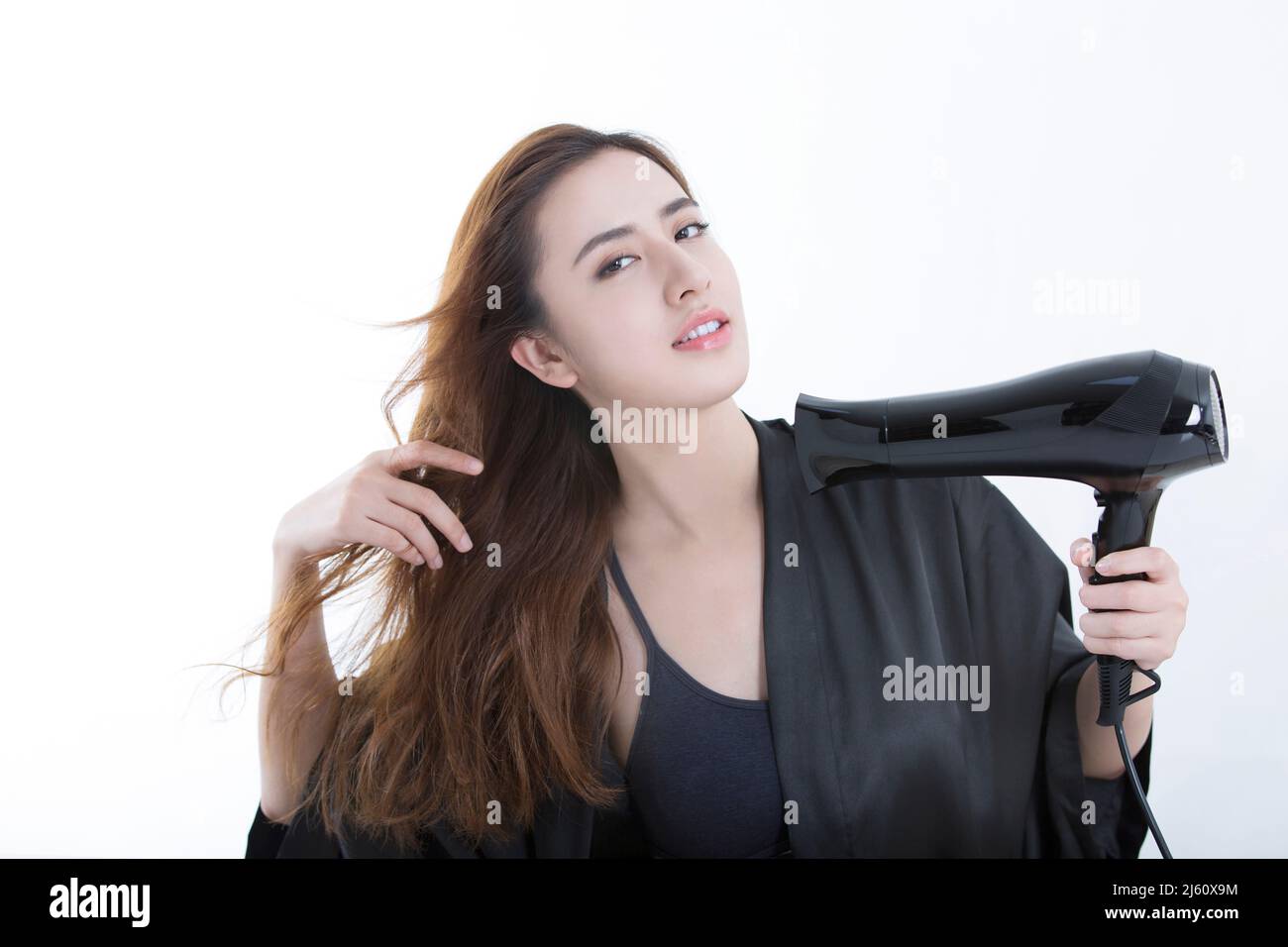 Jeune et belle femme chinoise utilisant un sèche-cheveux pour sécher les cheveux, sur fond blanc - photo de stock Banque D'Images