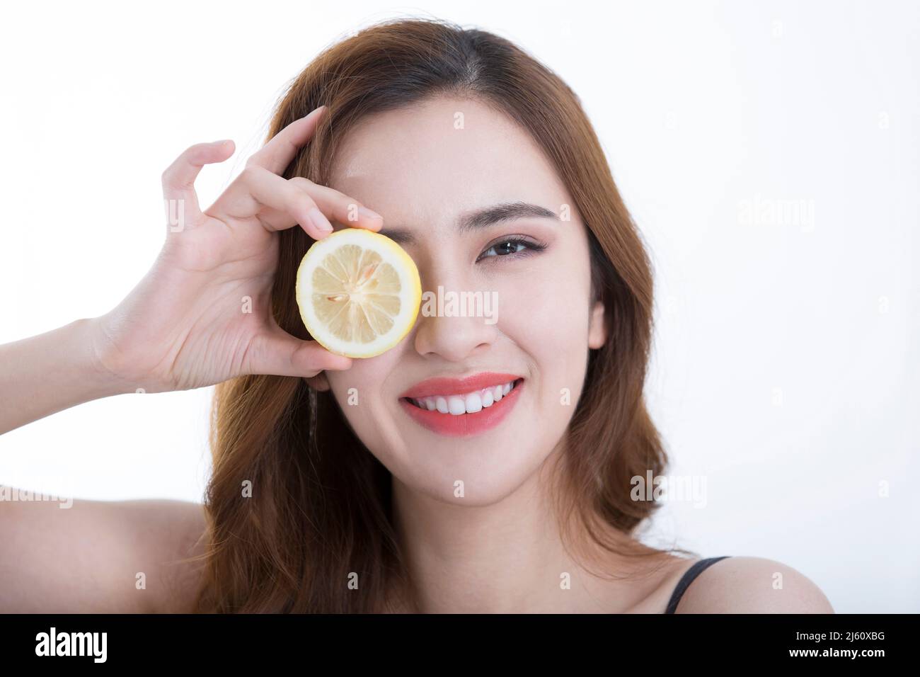 Jolie jeune dame a couvert ses yeux avec une tranche de citron, sur fond blanc - photo de stock Banque D'Images
