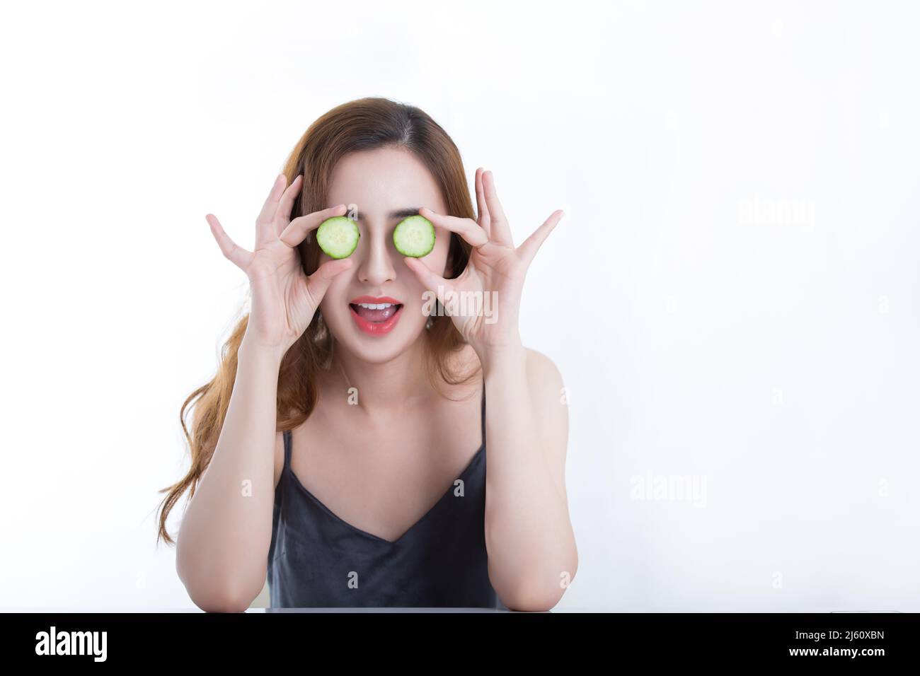 Jolie jeune dame a couvert ses yeux avec une tranche de concombre, sur fond blanc - photo de stock Banque D'Images