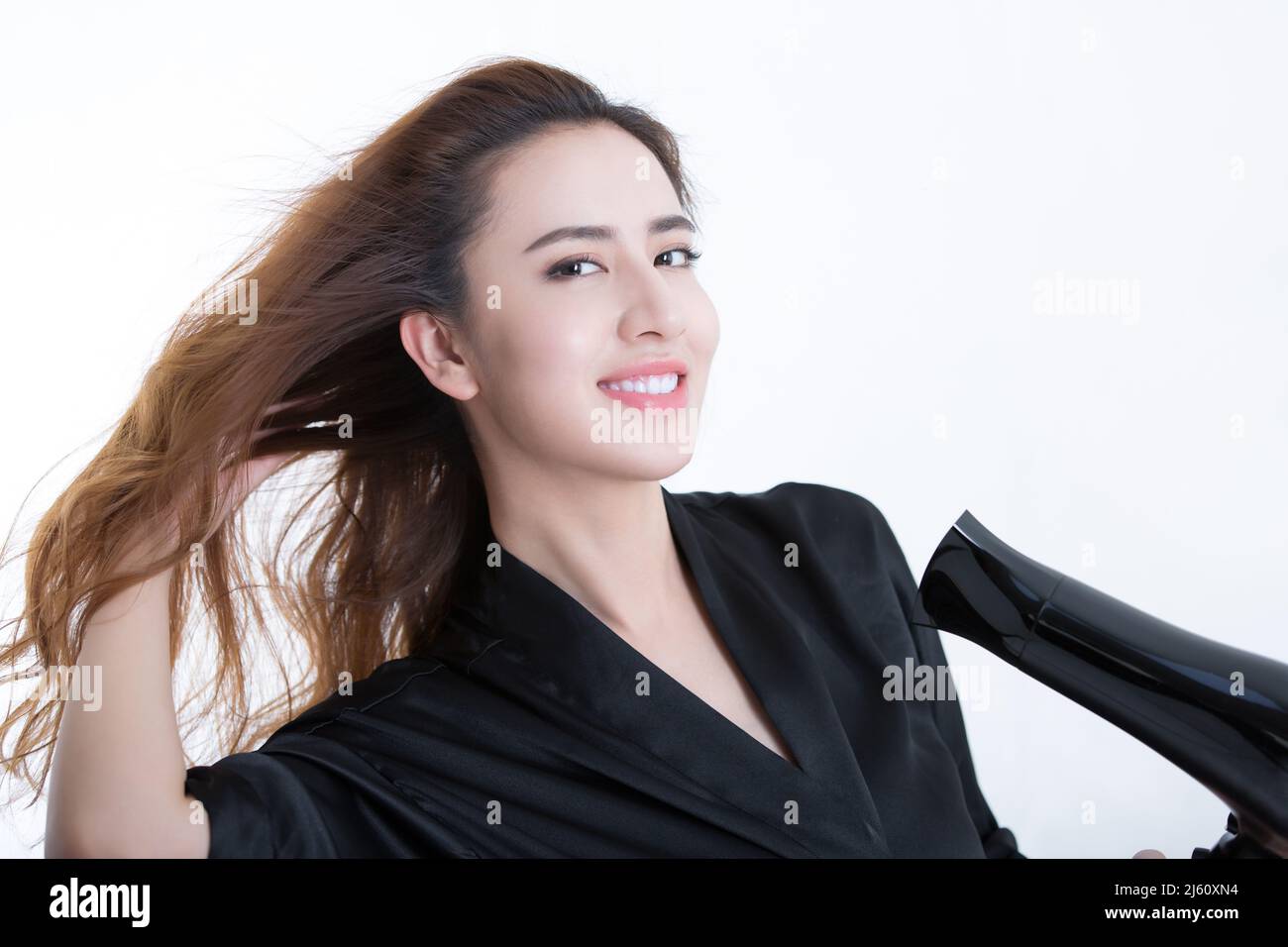 Jeune et belle femme chinoise utilisant un sèche-cheveux pour sécher les cheveux, sur fond blanc - photo de stock Banque D'Images