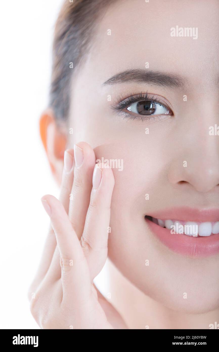 Jeune femme souriant comme elle se déplace sa peau lisse après l'application des produits de soin de peau, sur fond blanc - photo de stock Banque D'Images