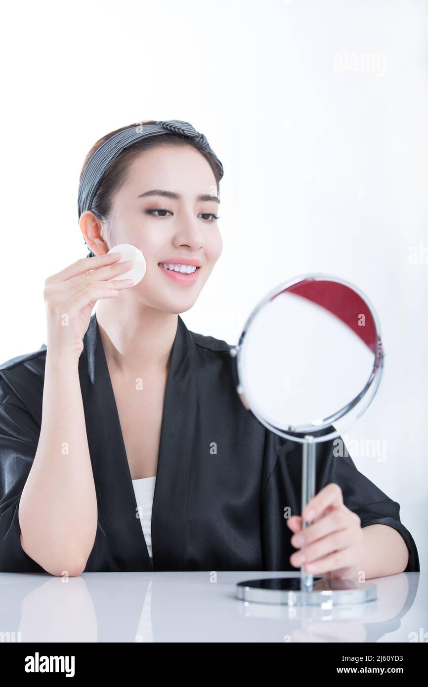 Jeune beauté se regardant dans un miroir est en utilisant une poudre pour se maquillage, sur fond blanc - photo de stock Banque D'Images