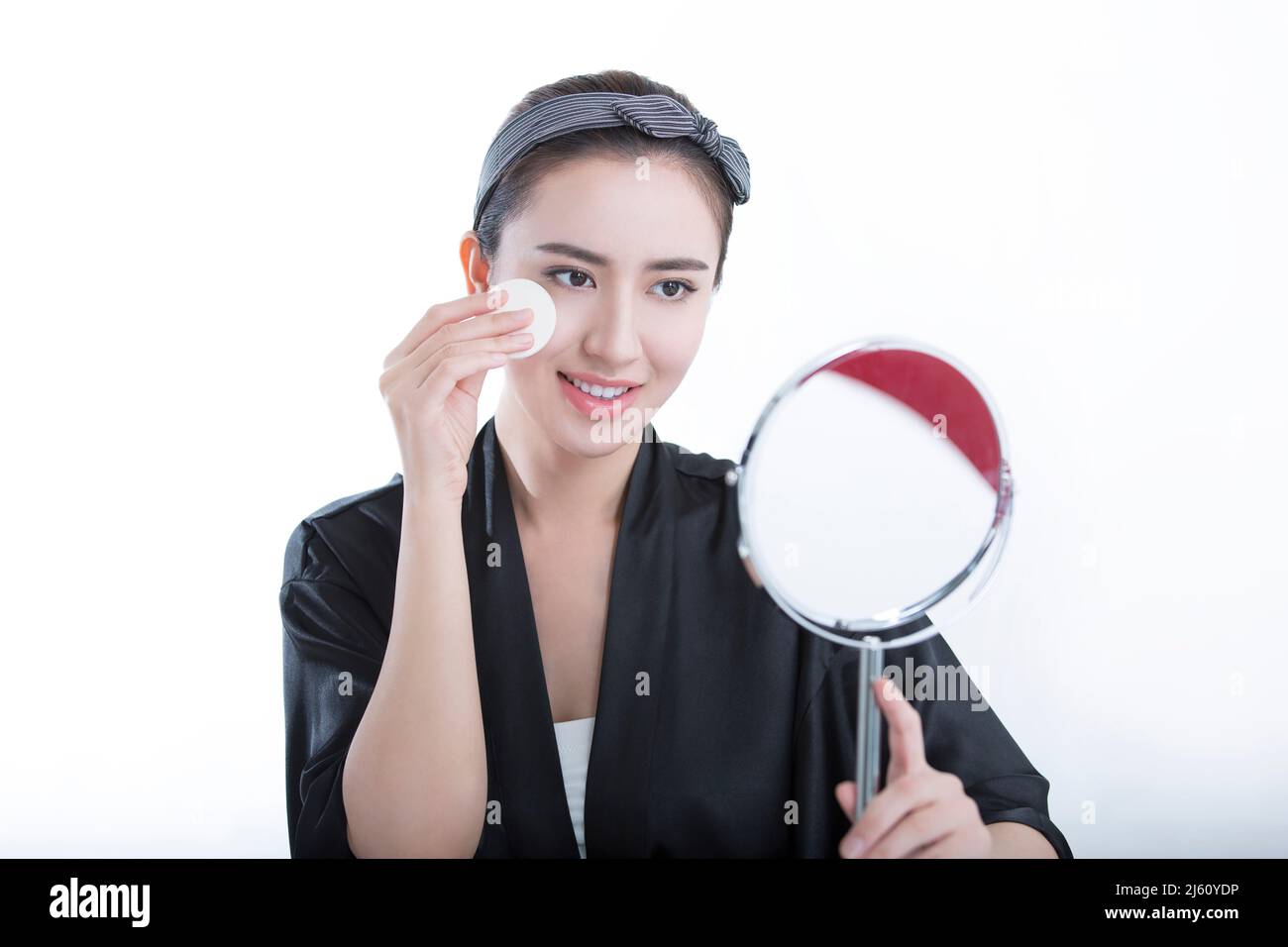 Jeune beauté se regardant dans un miroir est en utilisant une poudre pour se maquillage, sur fond blanc - photo de stock Banque D'Images