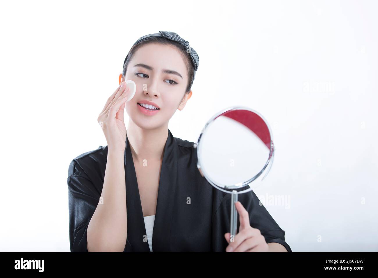 Jeune beauté se regardant dans un miroir est en utilisant une poudre pour se maquillage, sur fond blanc - photo de stock Banque D'Images