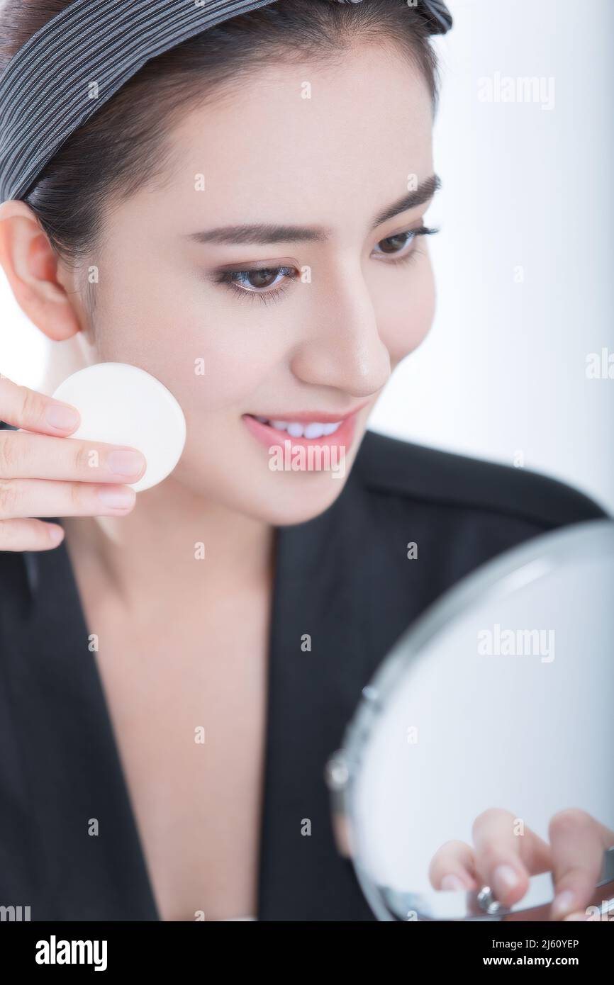 Jeune beauté en face d'un miroir de maquillage est l'application de poudre, sur fond blanc - photo de stock Banque D'Images