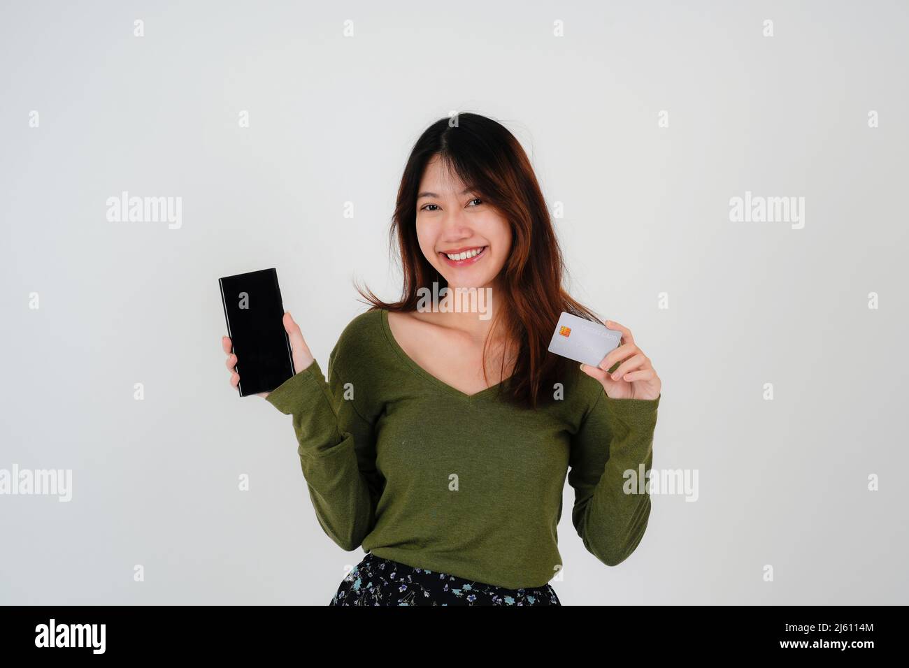 Image d'une belle jeune jolie femme posant isolée sur fond de mur blanc en utilisant le téléphone mobile tenant la carte de crédit. Banque D'Images