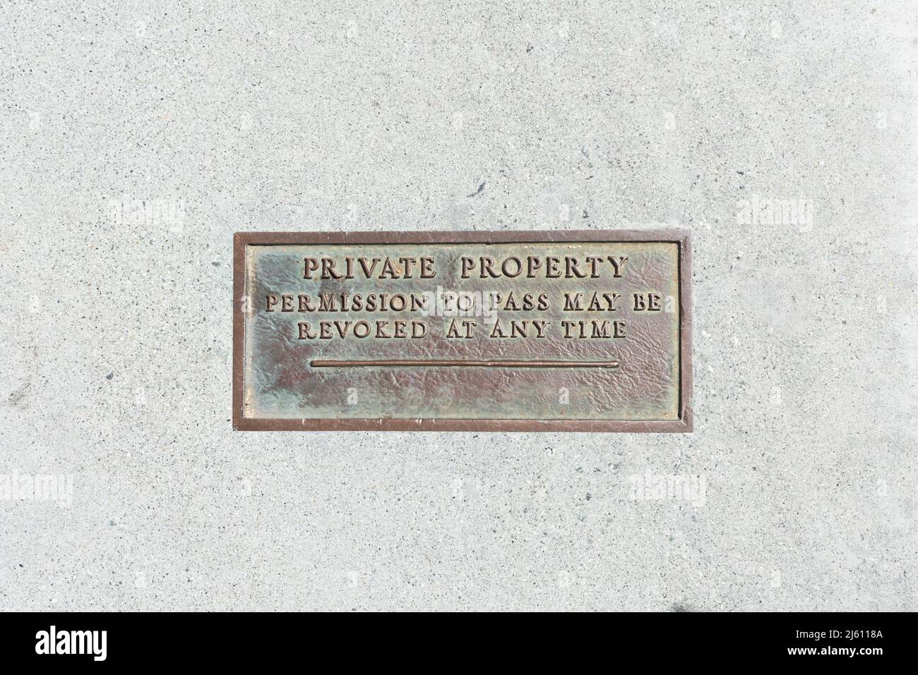 Propriété privée permission de passer peut être révoquée à tout moment signe métallique, plaque sur le trottoir en béton. Banque D'Images