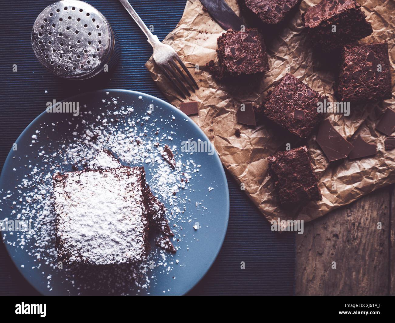 l'image montre un topview de brownies maison décored avec de la poudre de sucre sur table rustique en bois; quelques autres brownies sur papier de cuisson; shaker supplémentaire o Banque D'Images