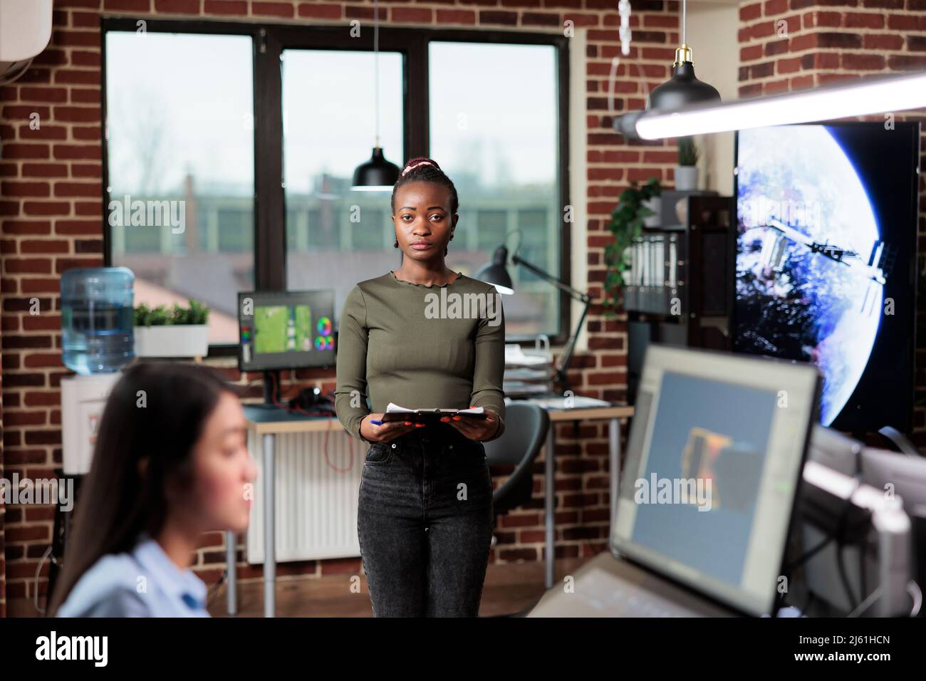 Employé de bureau d'agence créative debout dans l'espace de travail, regardant la caméra tout en ayant le presse-papiers. Département de production leader de l'équipe afro-américaine dans l'intérieur moderne. Banque D'Images