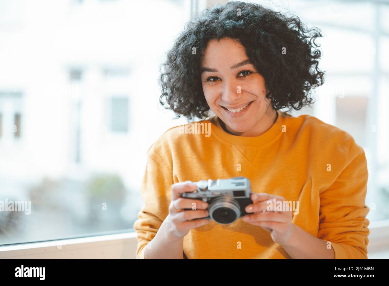 Femme souriante avec appareil photo assis près de la fenêtre à la maison Banque D'Images