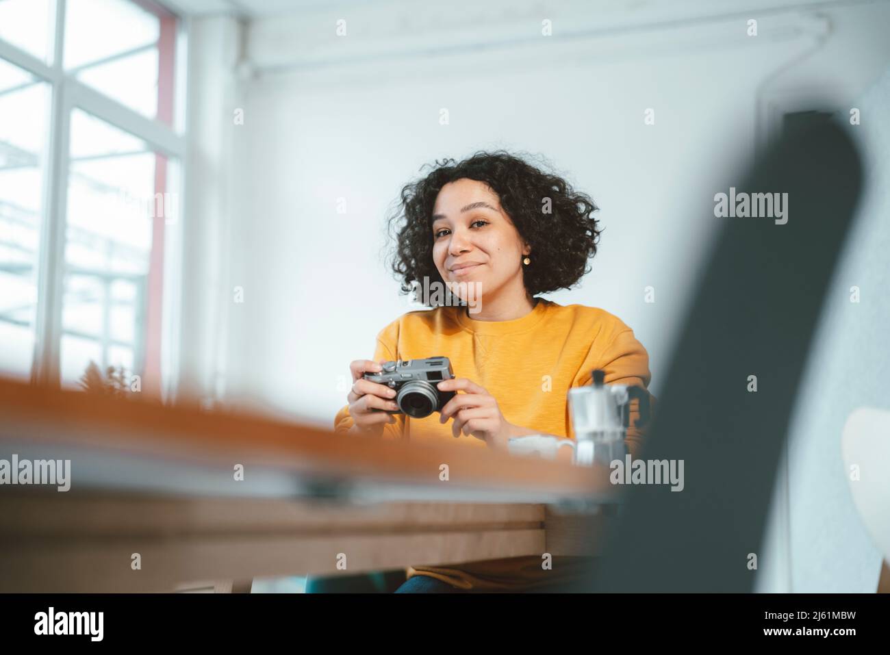 Femme souriante avec appareil photo assis à une table dans le salon Banque D'Images