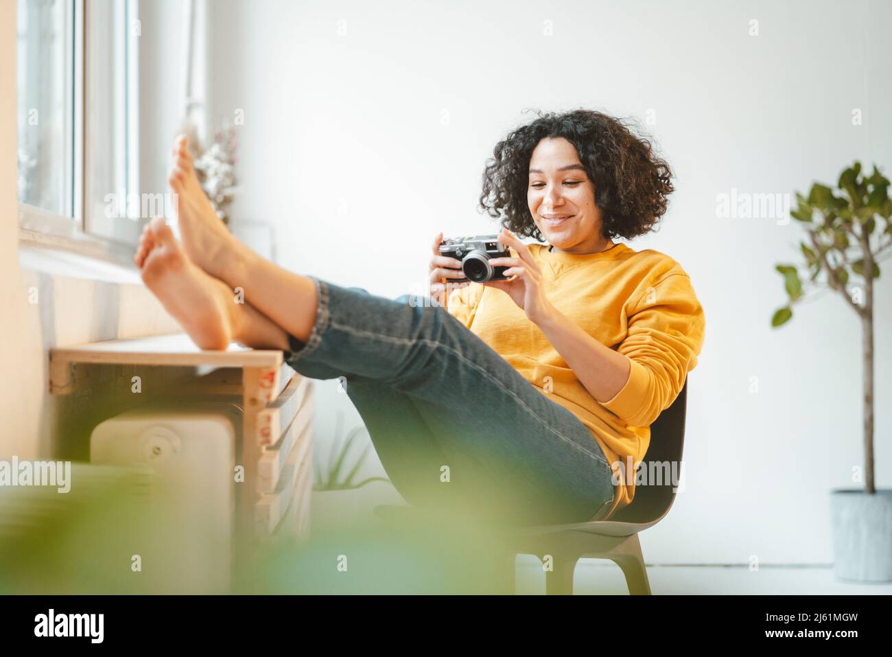Femme souriante avec caméra assise sur une chaise à la maison Banque D'Images