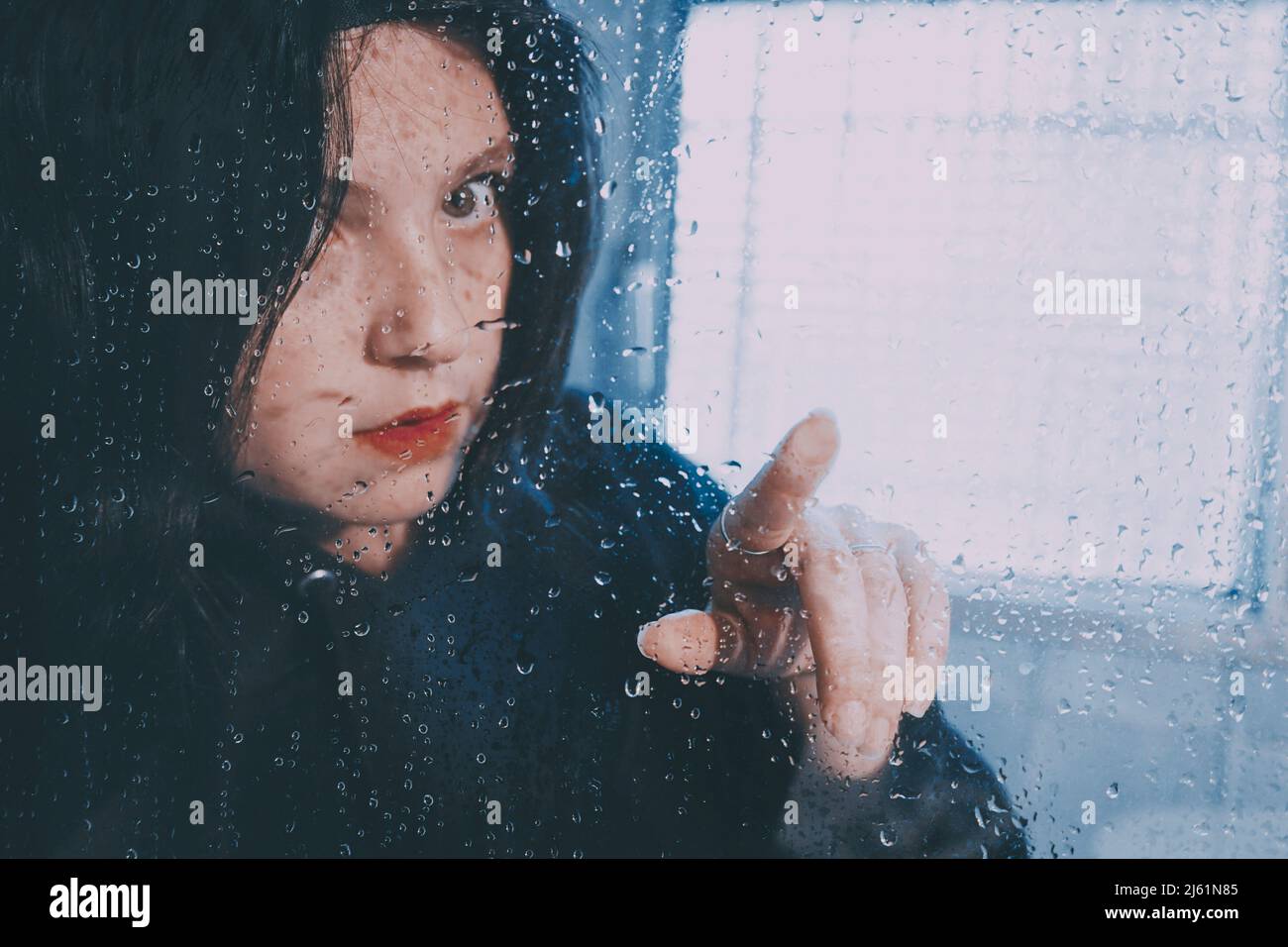 Femme aux cheveux noirs touchant le verre humide Banque D'Images